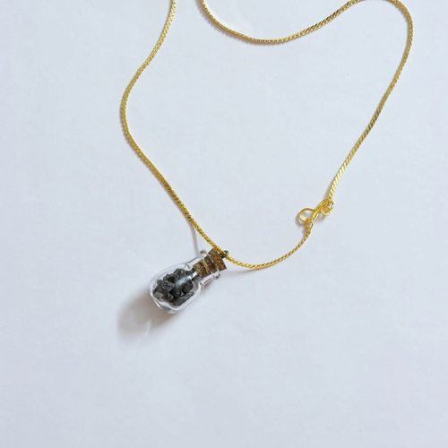Natchathiram meteorite vial pendant on gold chain, flat lay